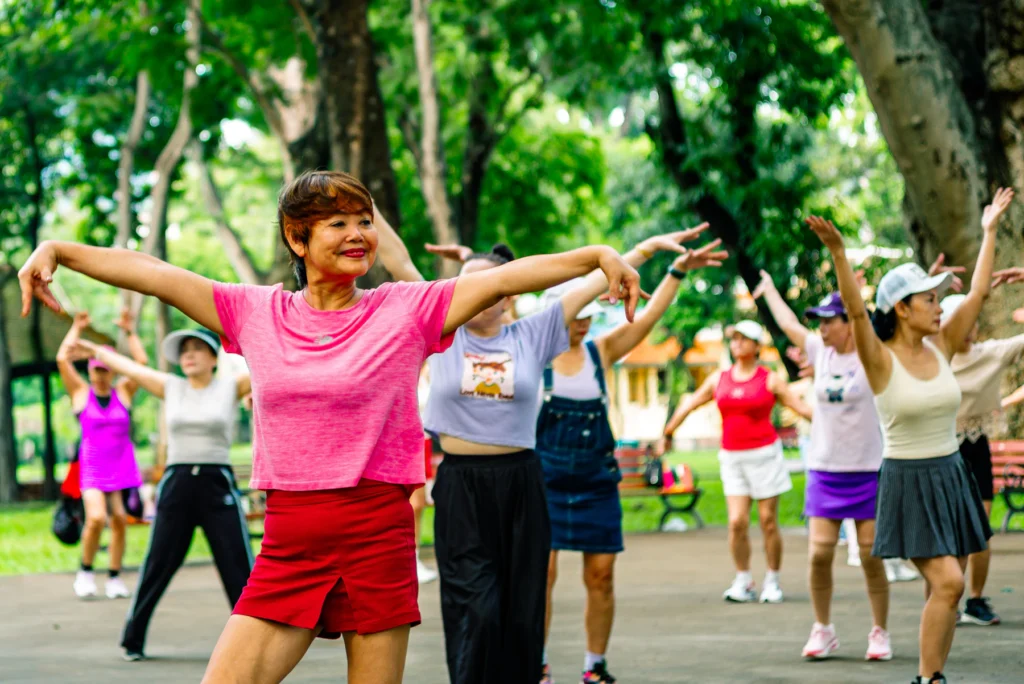 Group of older women doing balance exercises with arms outstretched in a park