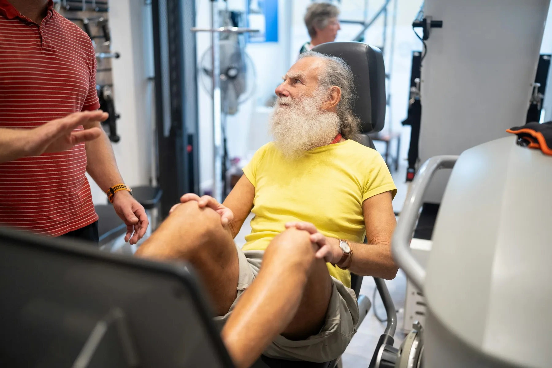 Older man doing leg press strength training with a trainer in a gym